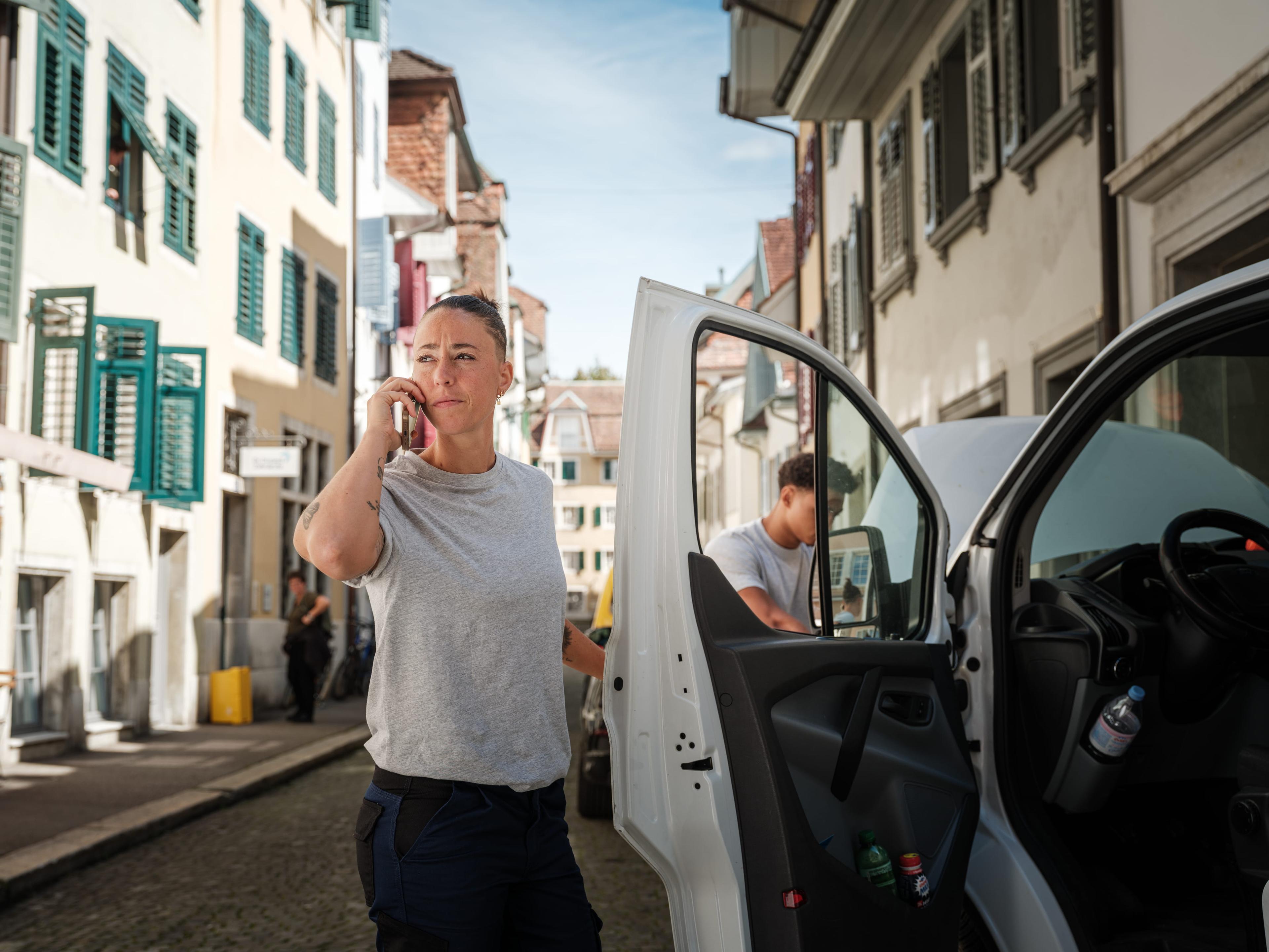 Handwerkerin telefoniert neben dem liegengebliebenen Firmenwagen